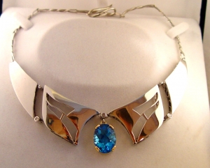 Ici, nous avons une topaze bleu sertie dans un chaton en or jaune entouré d'un collier en argent. Les systèmes de séparation des différents éléments sont sertis de petits diamants.